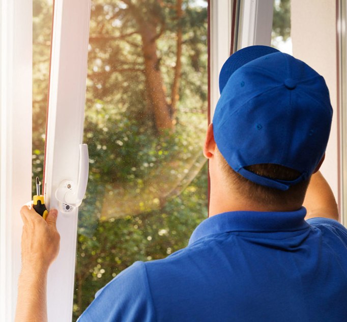 A Window Nation employee in a blue shirt and hat fixing a window