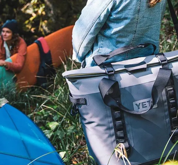 A person outdoors carrying a blue YETI cooler